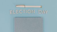 Blue notebook and pen against a light blue background reading 'Election Day', ideal for campaign themes.